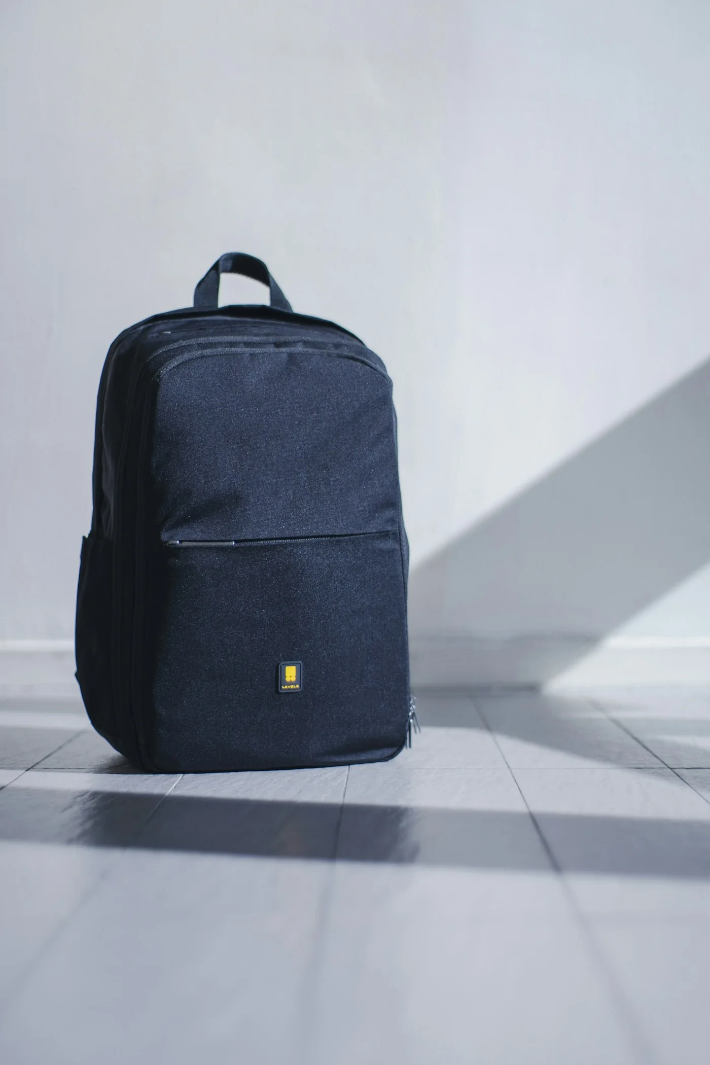 Dark compact backpack against a pale wall